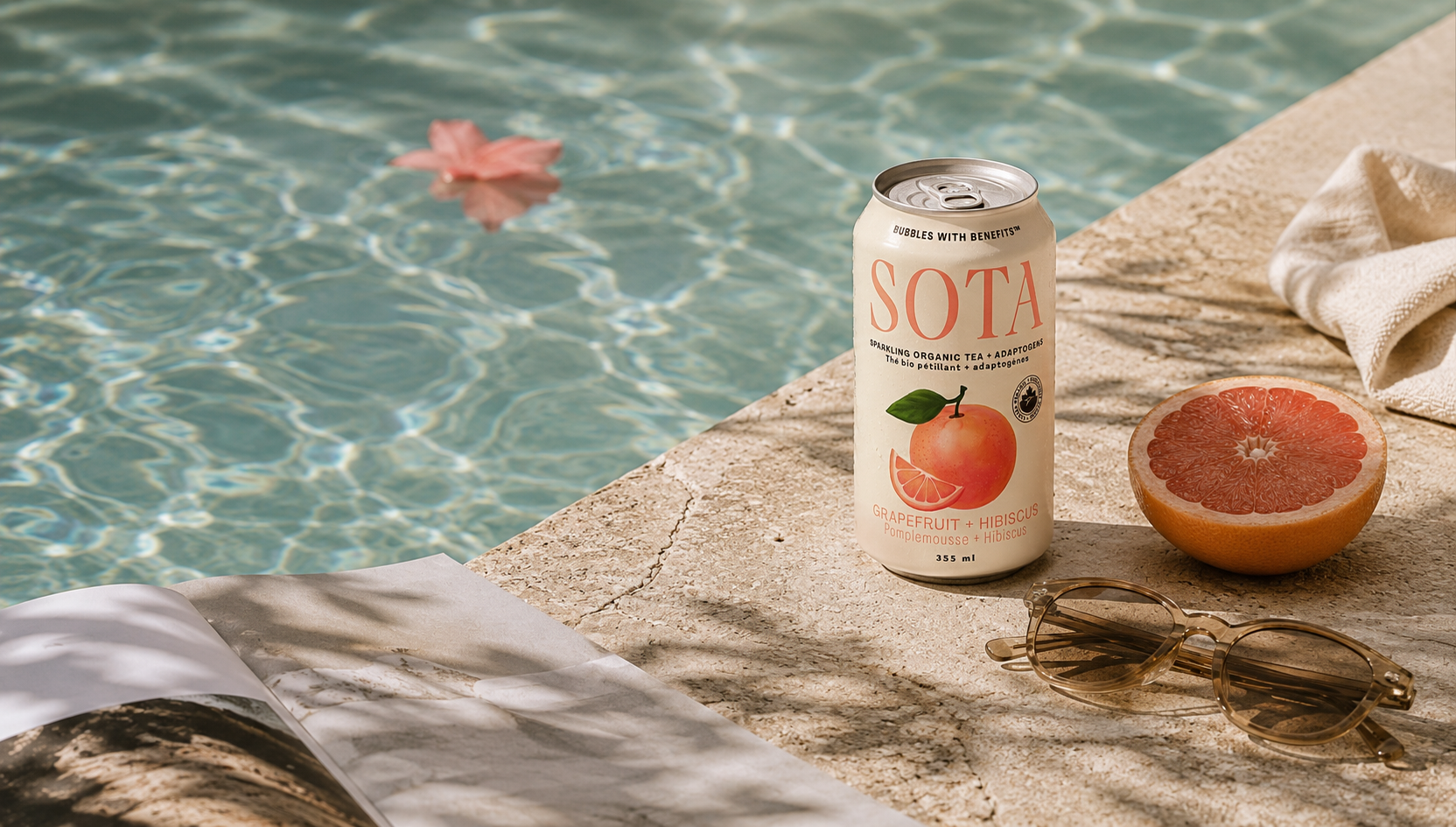 Soda can with grapefruit on a poolside ledge with sunglasses and a towel.